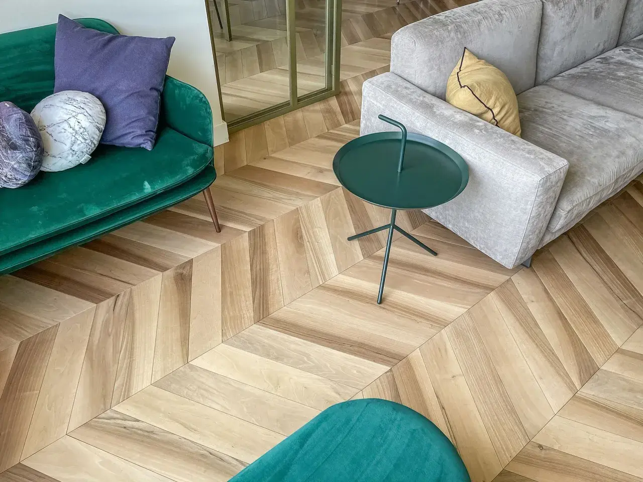 Un elegante soggiorno con un pavimento stile nordico a spina di pesce. Divani verdi e grigi, tavolino verde e cuscini decorativi.