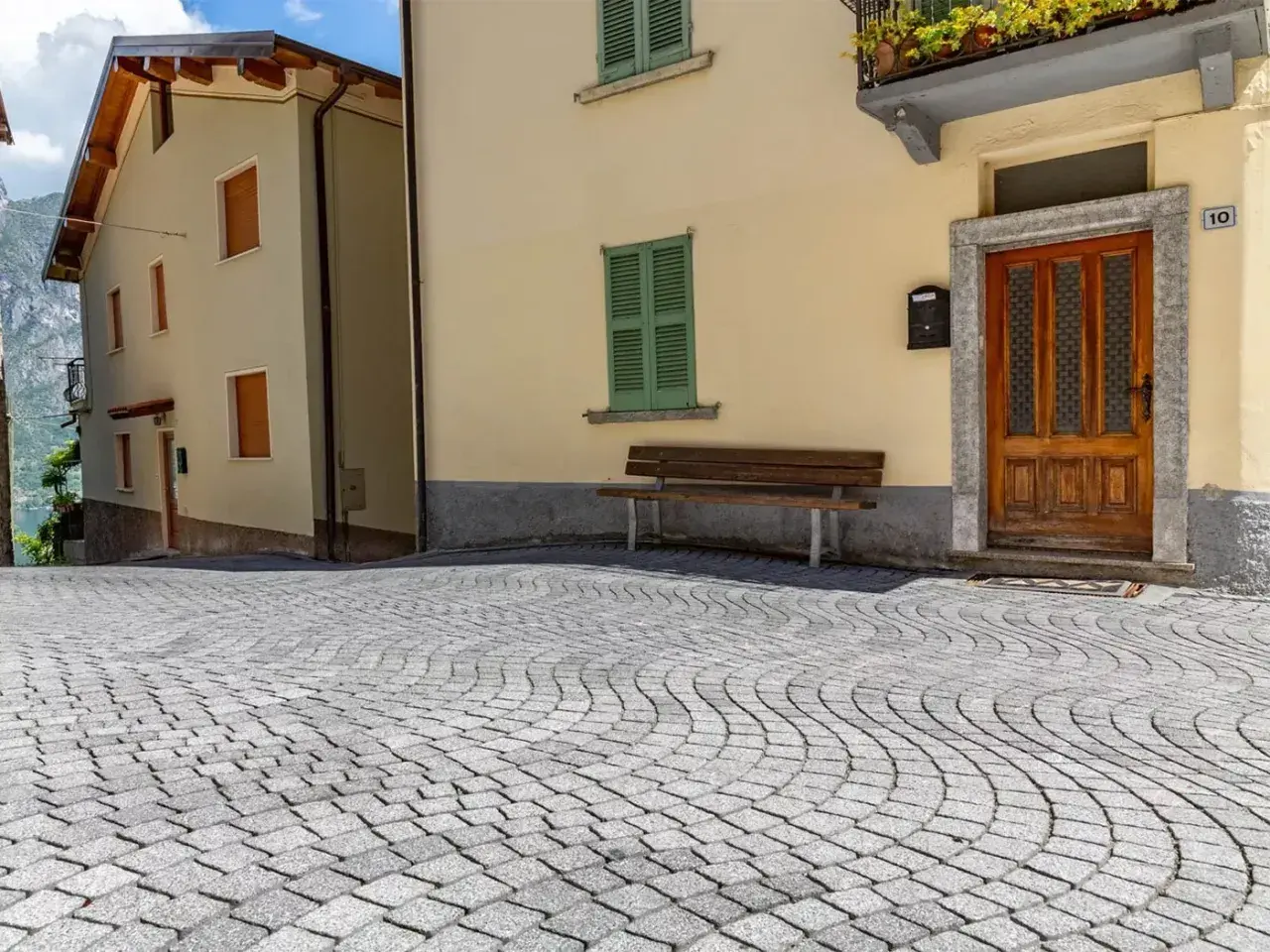Pavimentazione in pietra per esterni carrabili, con case color pastello e un panchina.