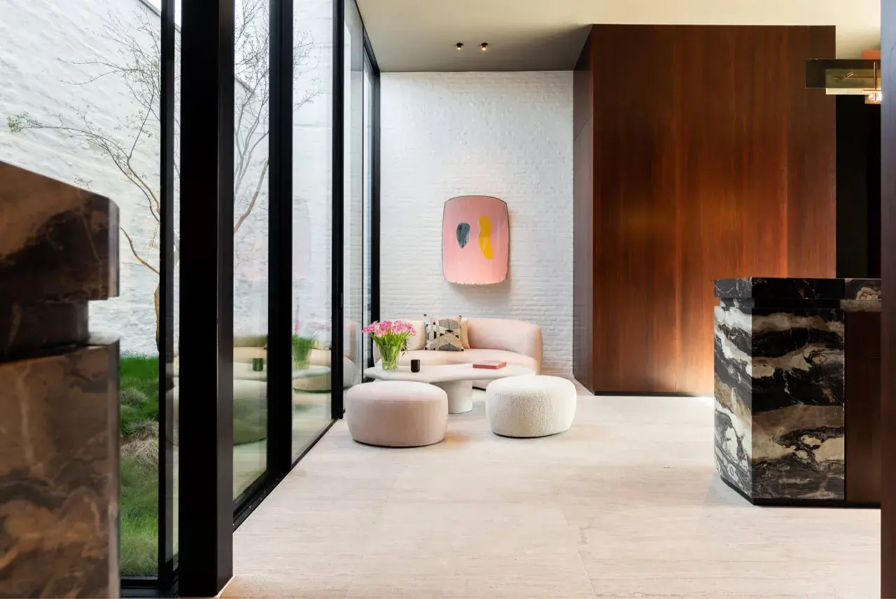 Un elegante soggiorno con pavimenti in marmo moderni, divano rosa, pouf e un tavolino bianco.