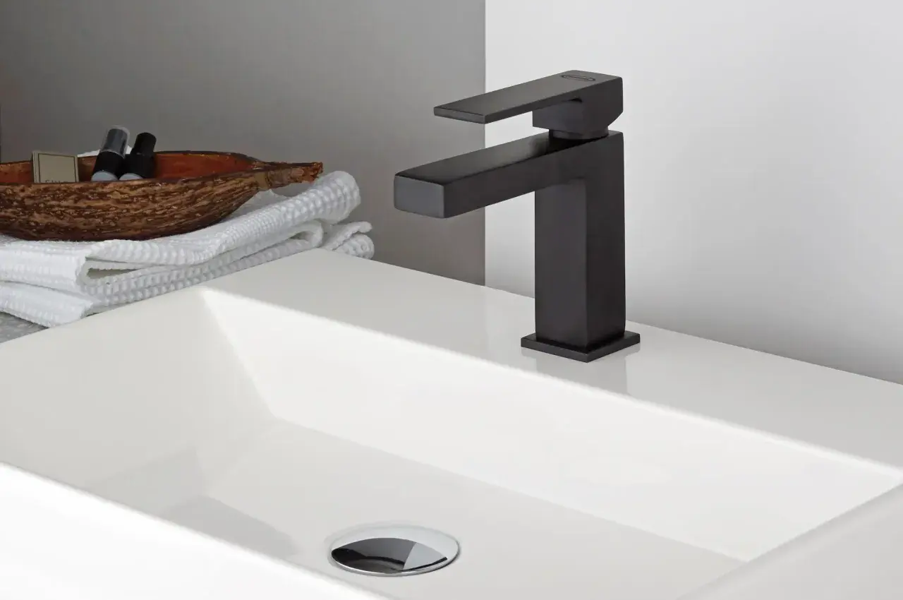 Lavabo bianco moderno con rubinetteria nera opaca. Accanto, asciugamani bianchi e una ciotola con prodotti da bagno.