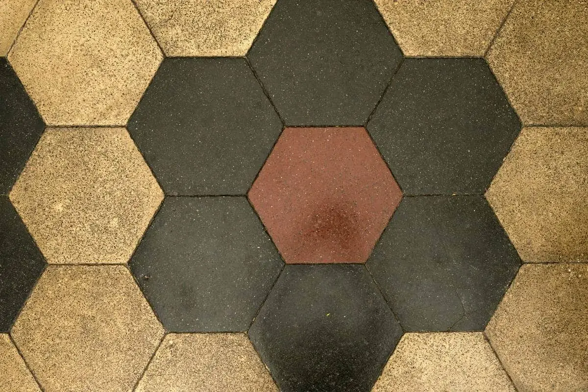 Pavimentazione a nido d'ape con cementine esagonali color ocra, grigio scuro e un tocco di rosso.