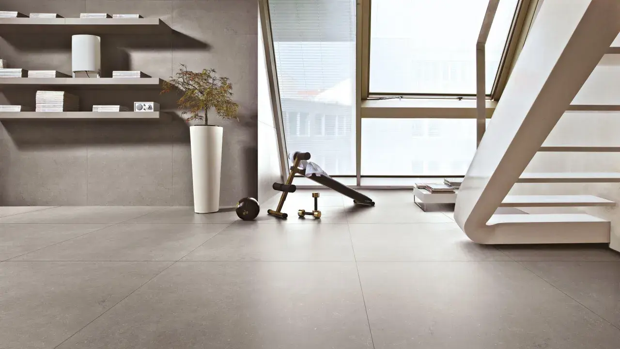 Pavimenti in kerlite per esterni, un angolo fitness con panca e pesi, scaffali con libri e una pianta in vaso.