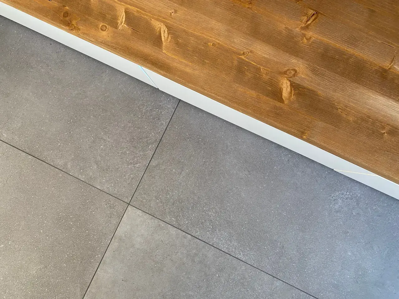 Le piastrelle grigie con venature sottili si incontrano sotto un piano in legno scuro, creando un contrasto moderno.