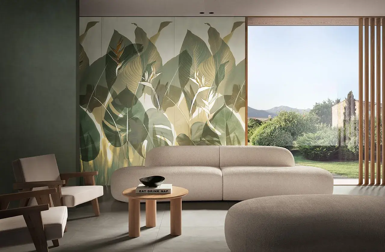 Soggiorno con divano beige e poltrone in legno, parete con fap rivestimenti a tema foglie tropicali e vista su giardino lussureggiante.