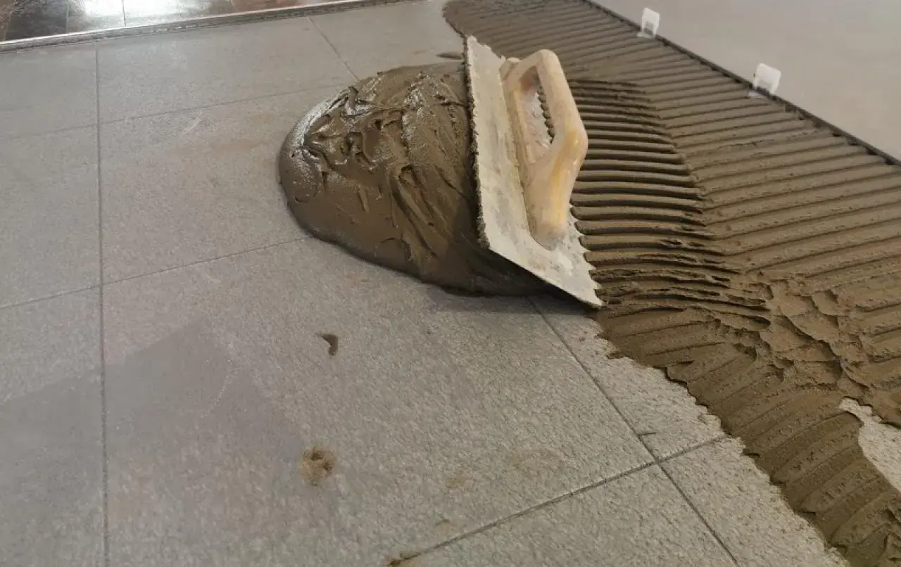 Cazzuola stende cemento per incollare piastrelle grigie. Lavoro in corso.