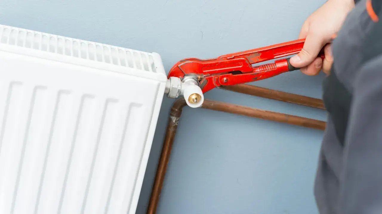 Un idraulico usa una chiave per regolare il raccordo di un termosifone bianco, mostrando come si misura interasse termosifoni per un'installazione corretta.