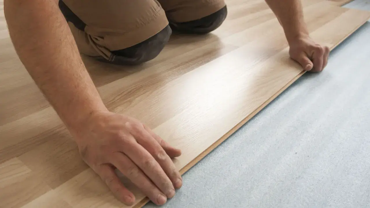 Mani esperte posano un nuovo pavimento in laminato chiaro su un sottofondo grigio. Si può posare gres su parquet, ma questo è un altro tipo di installazione.