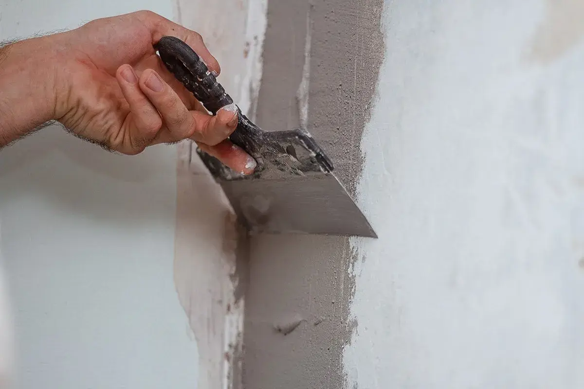 Mano usa una spatola per applicare materiale per chiudere buchi nel muro.