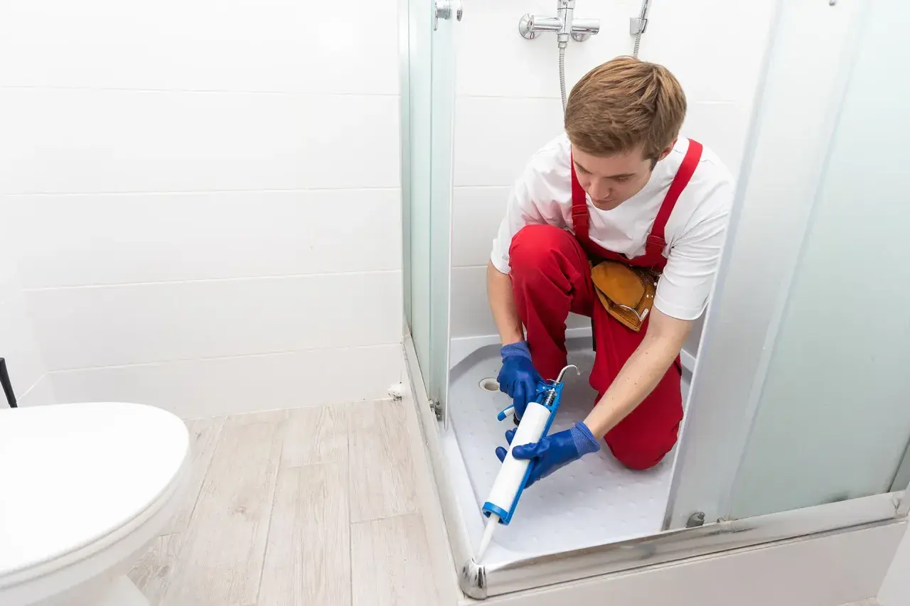 Installatore usa silicone per box doccia, sigillando la base per prevenire perdite d'acqua.