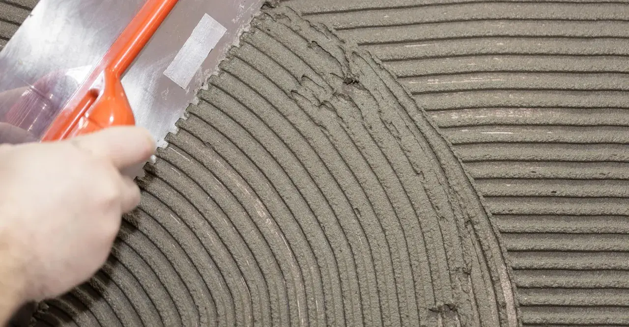 Una spatola dentata stende la colla per piastrelle su una superficie, creando righe uniformi per una posa perfetta.