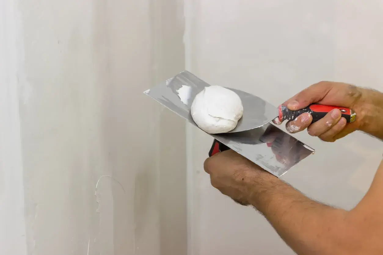 Mani esperte pronte a stuccare muro con spatola e stucco bianco.