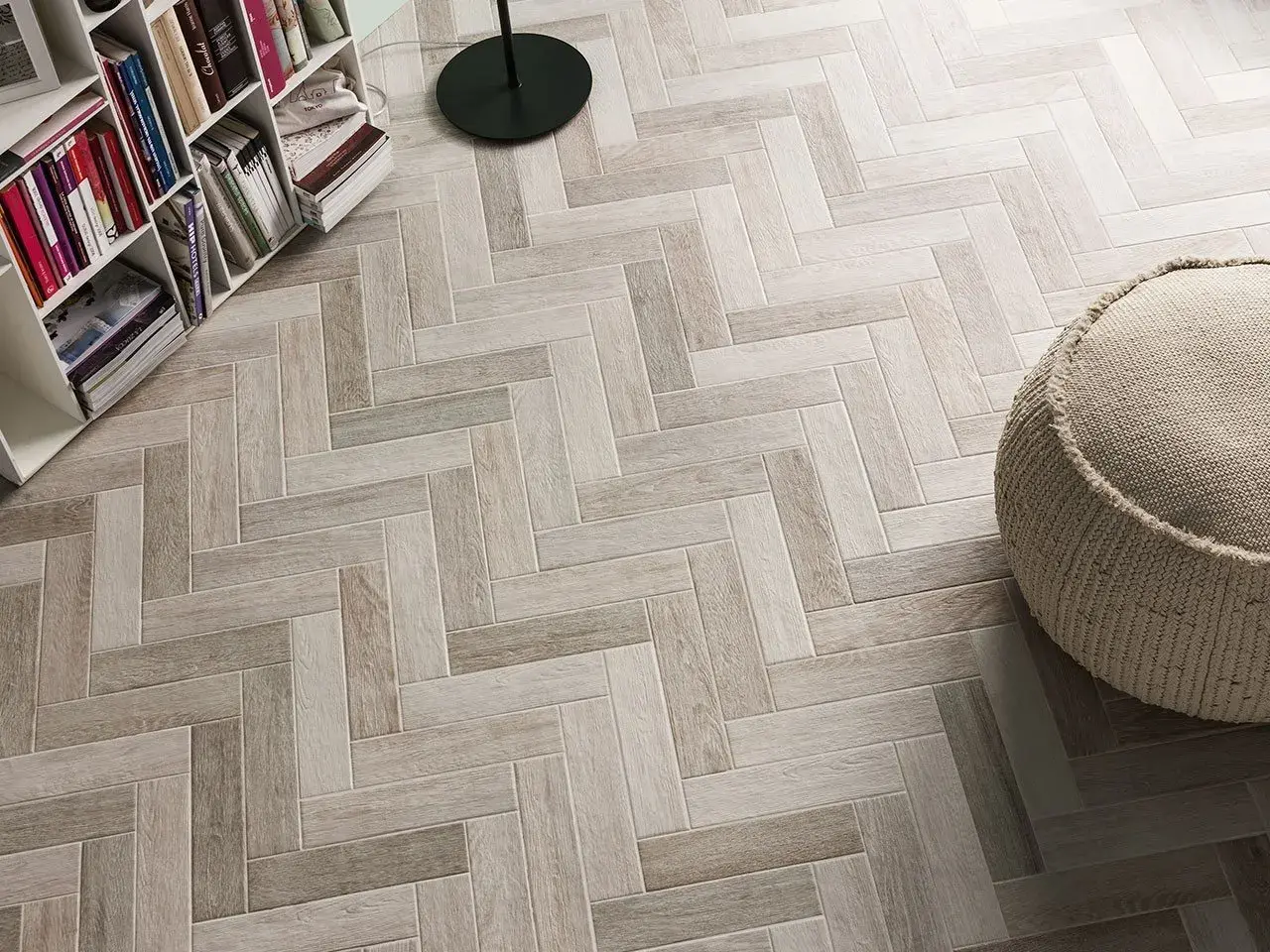 Un elegante pavimento ruvido interno in parquet a spina di pesce, con una libreria e un pouf.