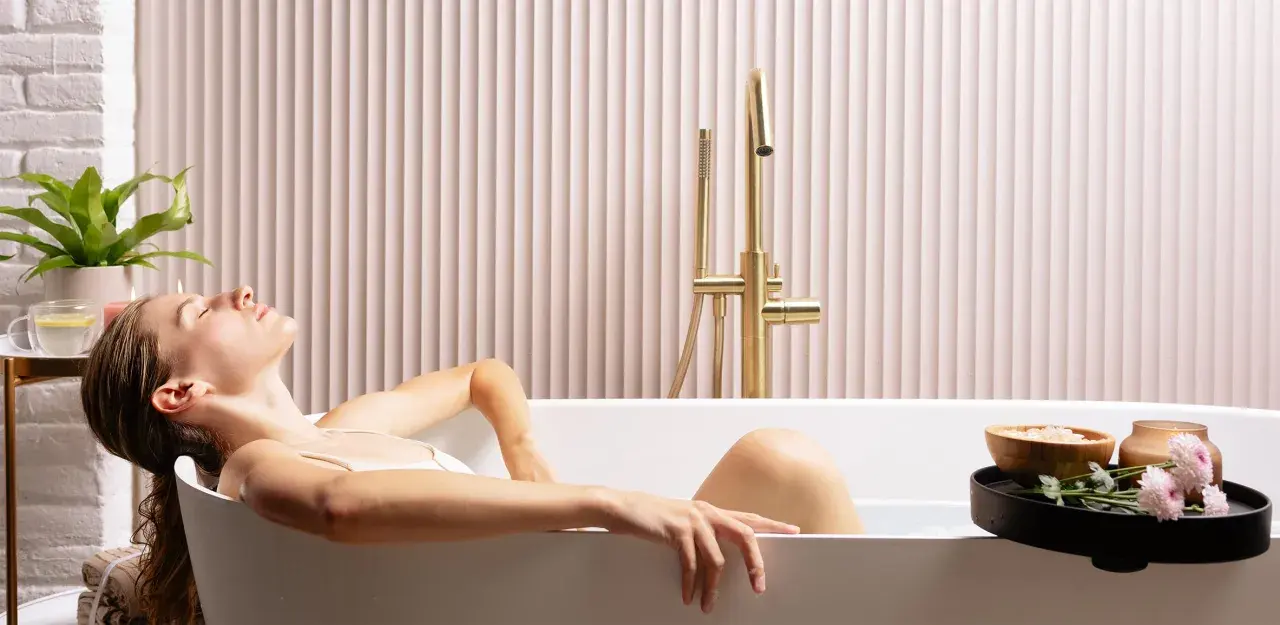 Donna rilassata in una vasca da bagno, creando un'atmosfera da bagno effetto spa con candele e fiori.
