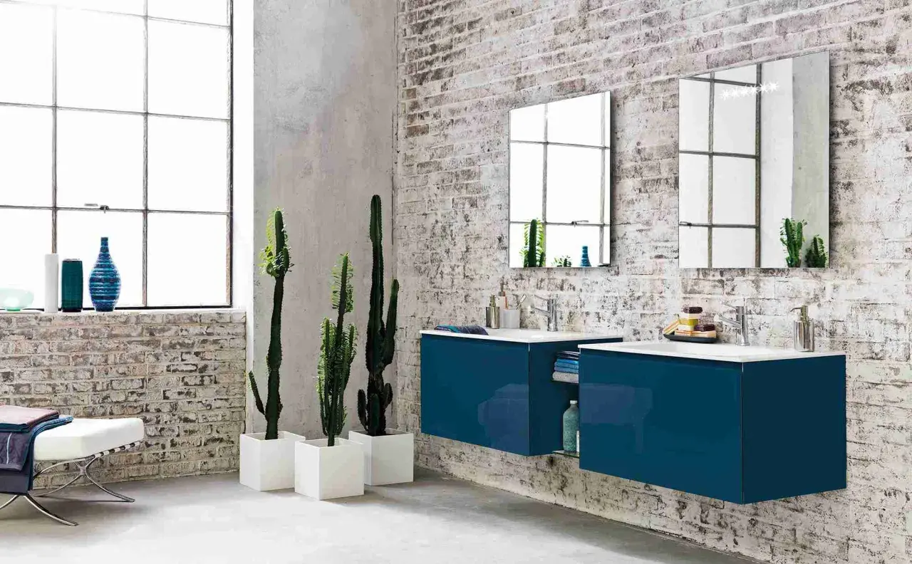 Bagno moderno con mattoni a vista, piante di cactus e mobili sospesi blu. Diversi tipi di piastrelle per un look industriale.