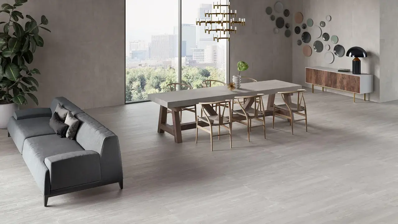 Un elegante soggiorno con divano grigio, tavolo da pranzo in cemento e sedie in legno, il tutto su un pavimento in gres porcellanato ruvido che evoca un'atmosfera moderna e accogliente.