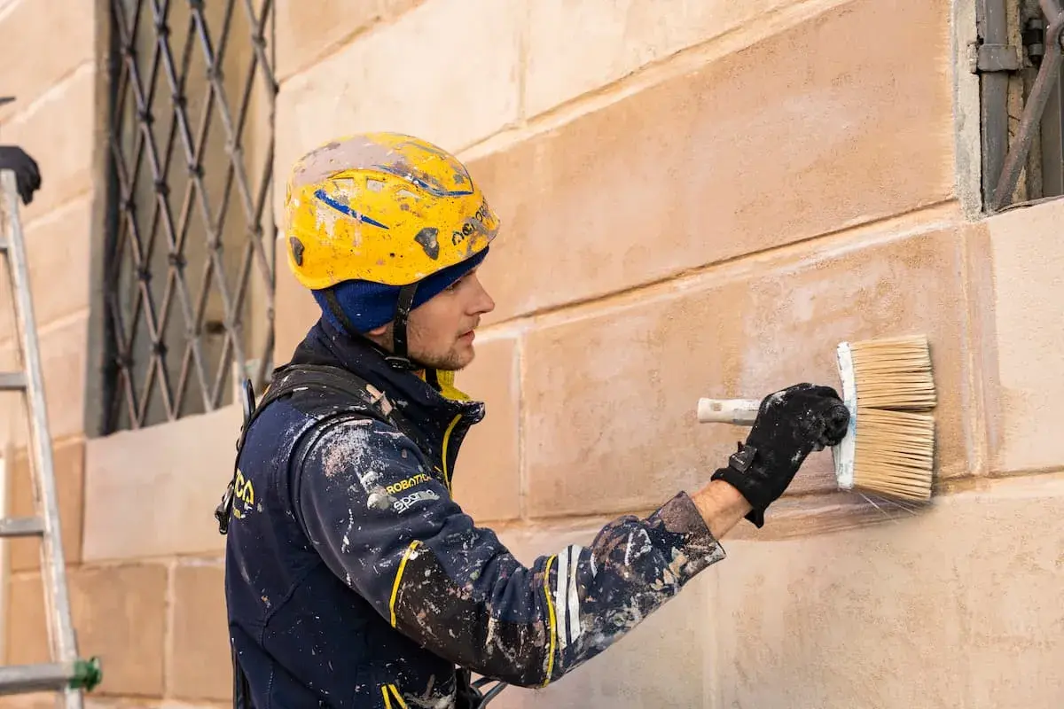 Operaio con casco giallo applica intonaco a un muro, un'alternativa alla rasatura dei muri per un nuovo look.
