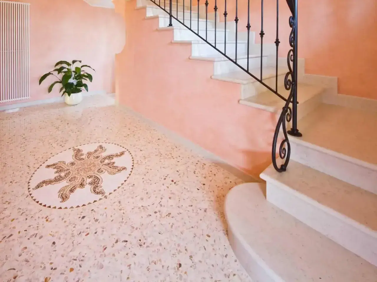 Un elegante pavimento veneziana con un mosaico centrale a forma di sole, accanto a una scala in marmo con ringhiera in ferro battuto.