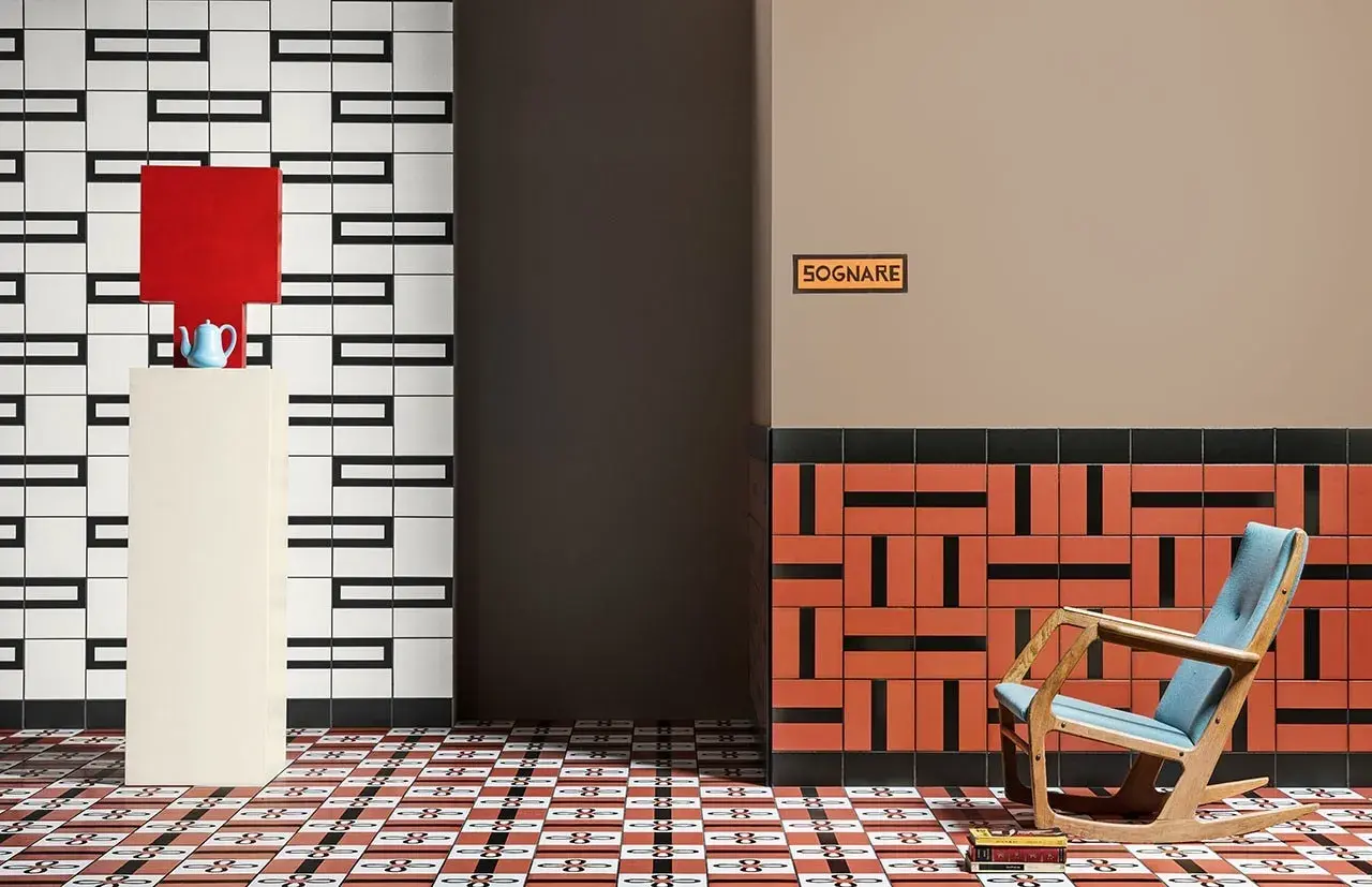 Un soggiorno moderno con pavimenti geometrici. Una poltrona a dondolo blu e legno, un piedistallo con una lampada rossa e una teiera blu.