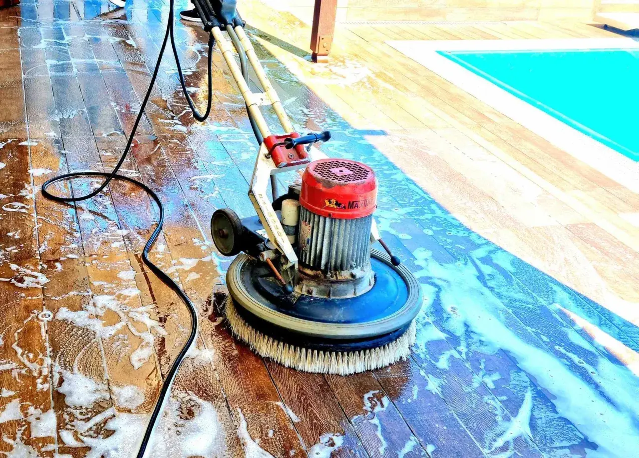 Macchina lavapavimenti in azione su un deck di legno, rimuovendo efficacemente la polvere di muratura e lo sporco, vicino a una piscina.