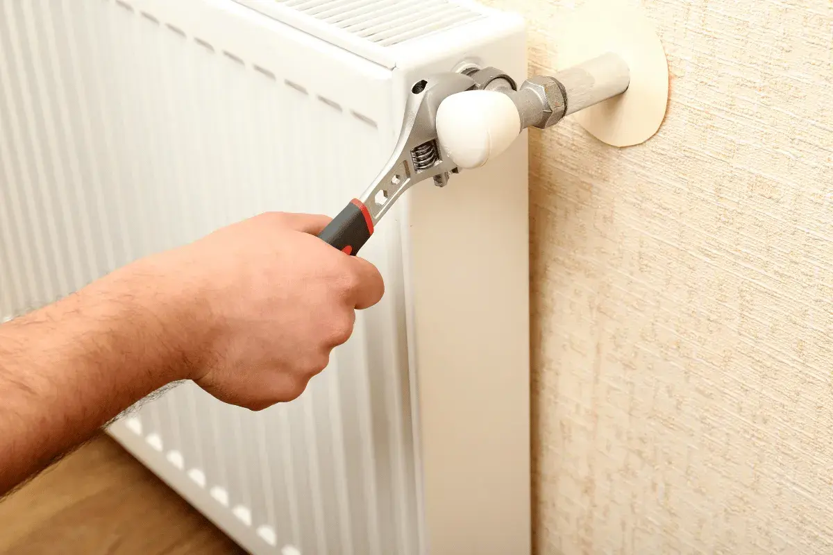 Mano con chiave inglese che regola un termosifone. L'aria nei termosifoni è un problema comune.