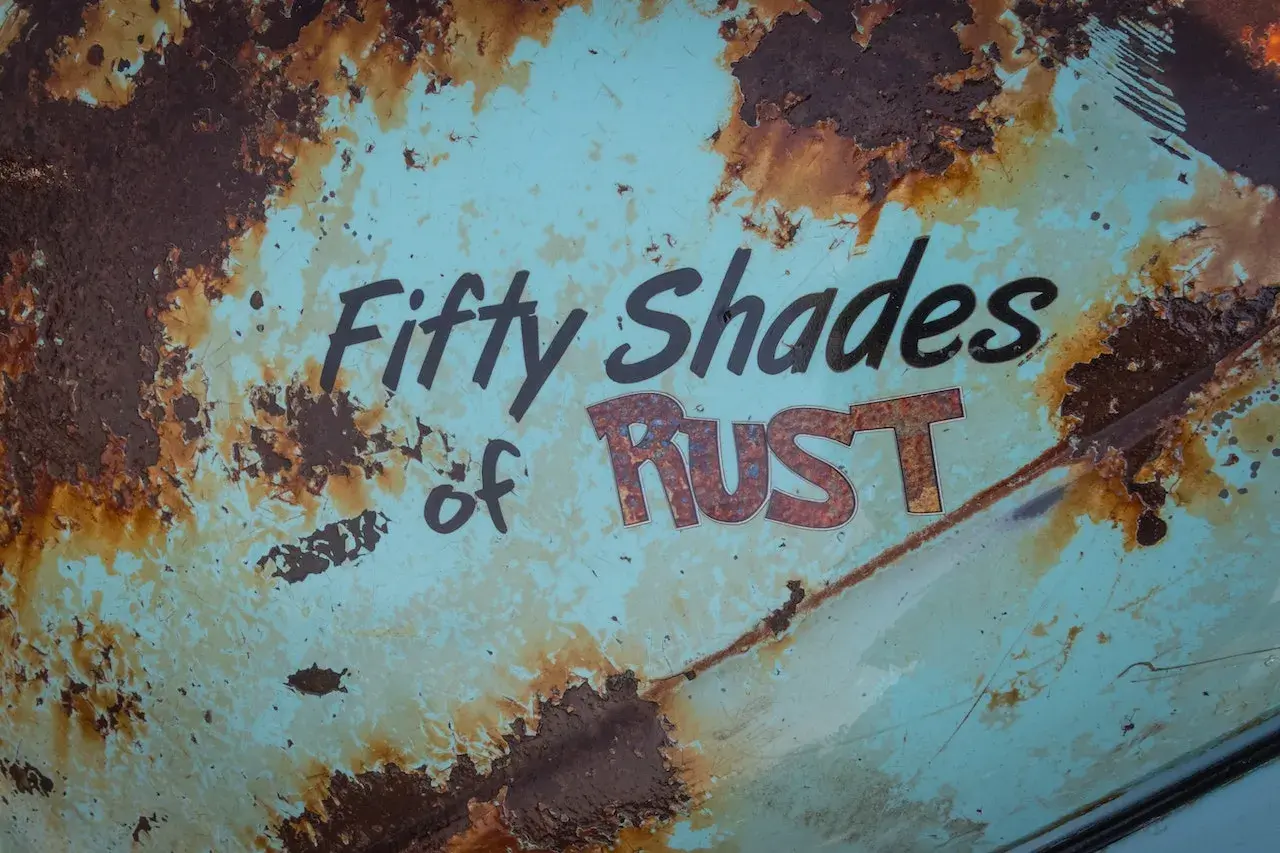 Superficie metallica sbiadita con scritte "Fifty Shades of RUST". La ruggine, che sembra voler togliere il colore originale, crea un effetto visivo intenso.