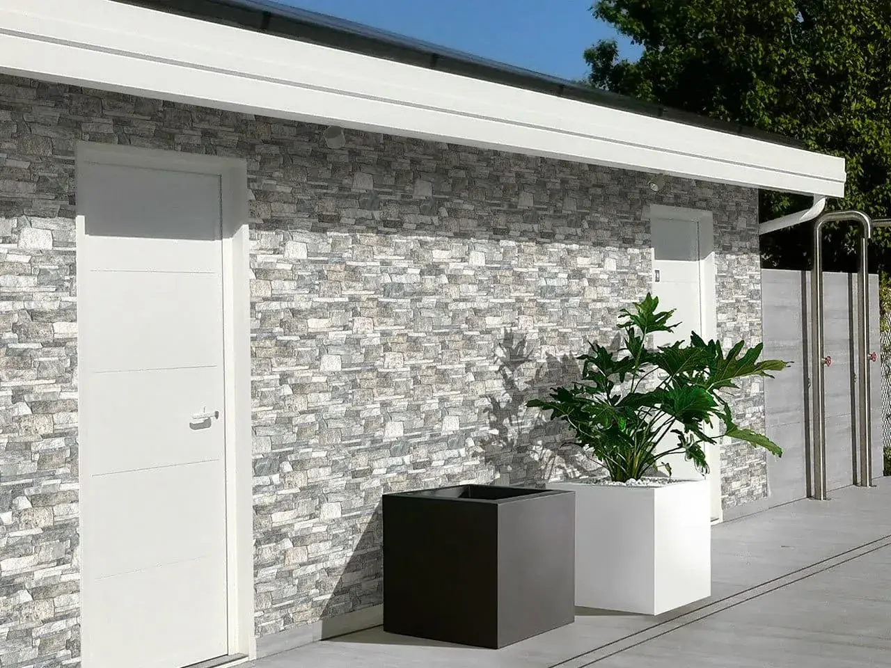 Muro esterno con rivestimento in pietra, che mostra diversi tipi di mattoni per muri esterni. Due porte bianche e fioriere moderne completano la scena.
