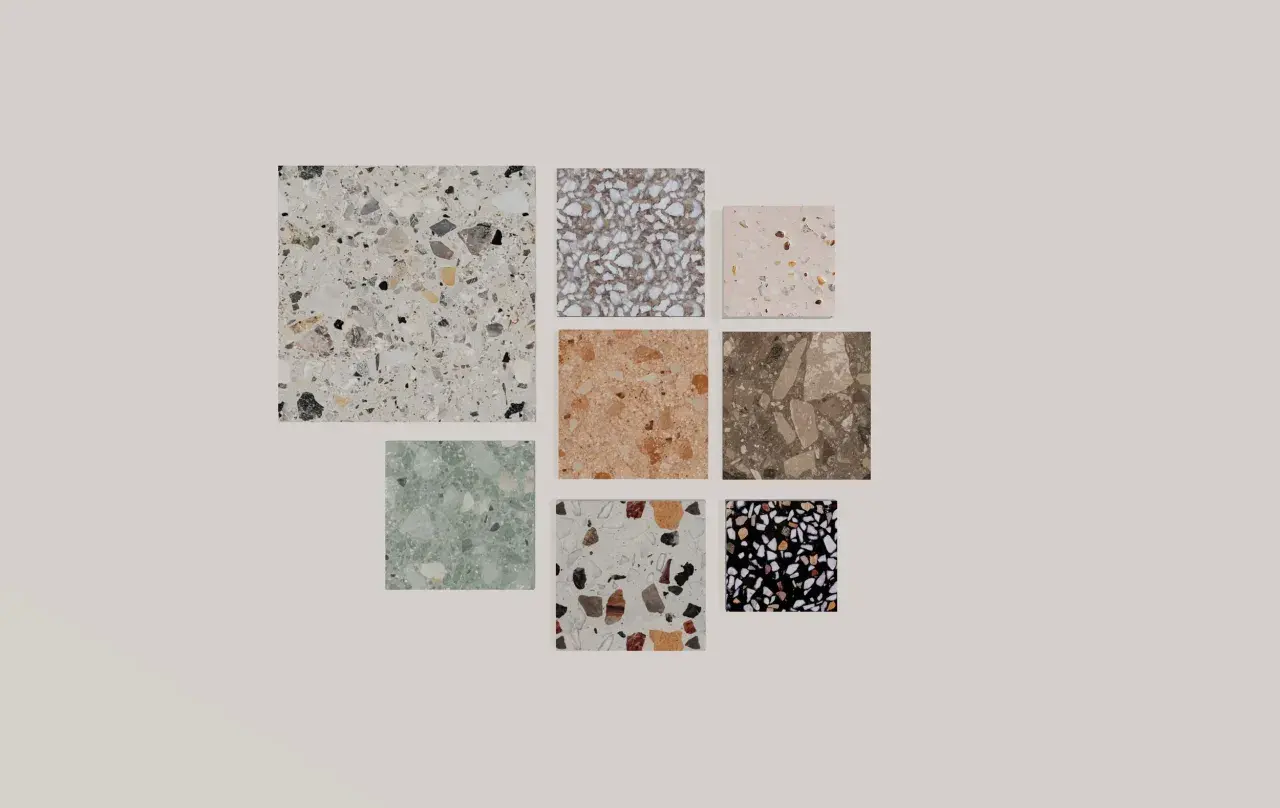 Vari campioni di piastrelle con un affascinante **effetto graniglia** in diverse colorazioni e dimensioni, dal bianco al nero, passando per tonalità naturali e pastello.