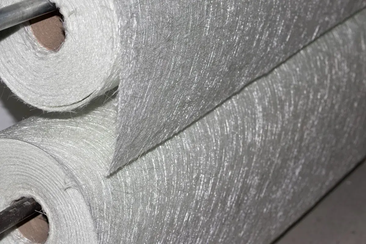 Rotoli di tessuto di fibra di vetro, materiale noto per la sua potenziale fibra di vetro cancerogena, con filamenti sottili e lucidi visibili.