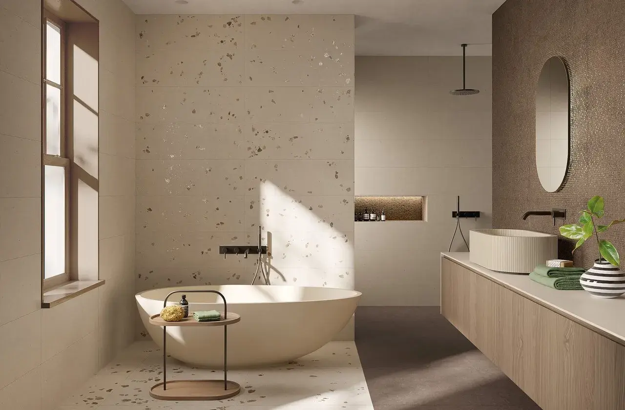 Bagno moderno con vasca freestanding e lavabo su mobile sospeso. Pareti e pavimento in fap gres porcellanato effetto terrazzo con inserti metallici.