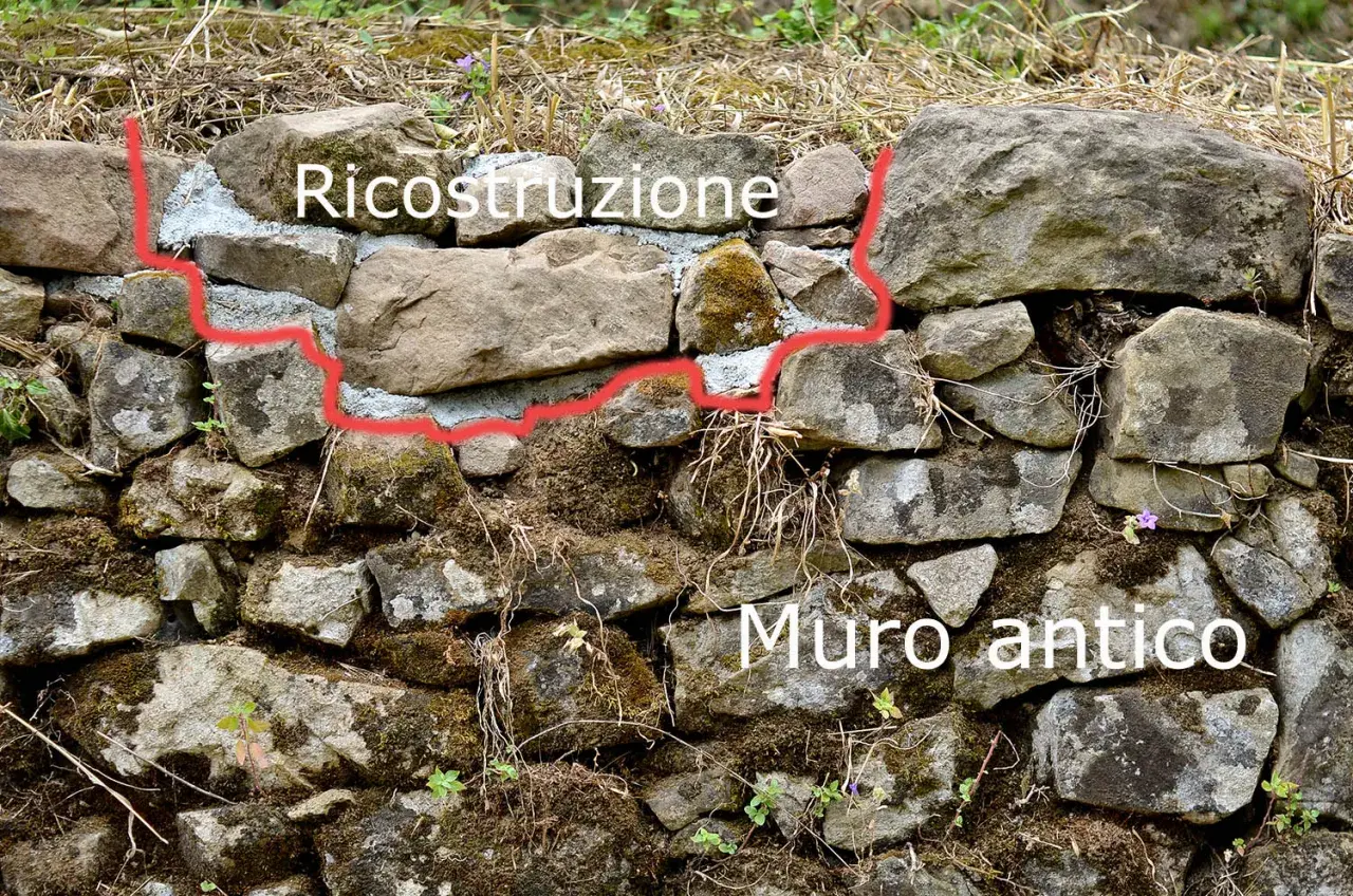 Ricostruzione di un muretto a secco antico, con pietre grezze e malta fresca che segna il confine tra vecchio e nuovo.