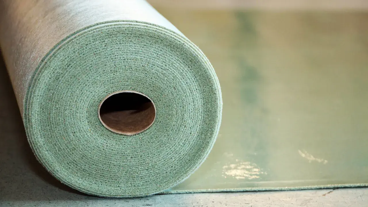 Rotolo di materiale per insonorizzare pavimento, con texture fibrosa e colore verde chiaro.