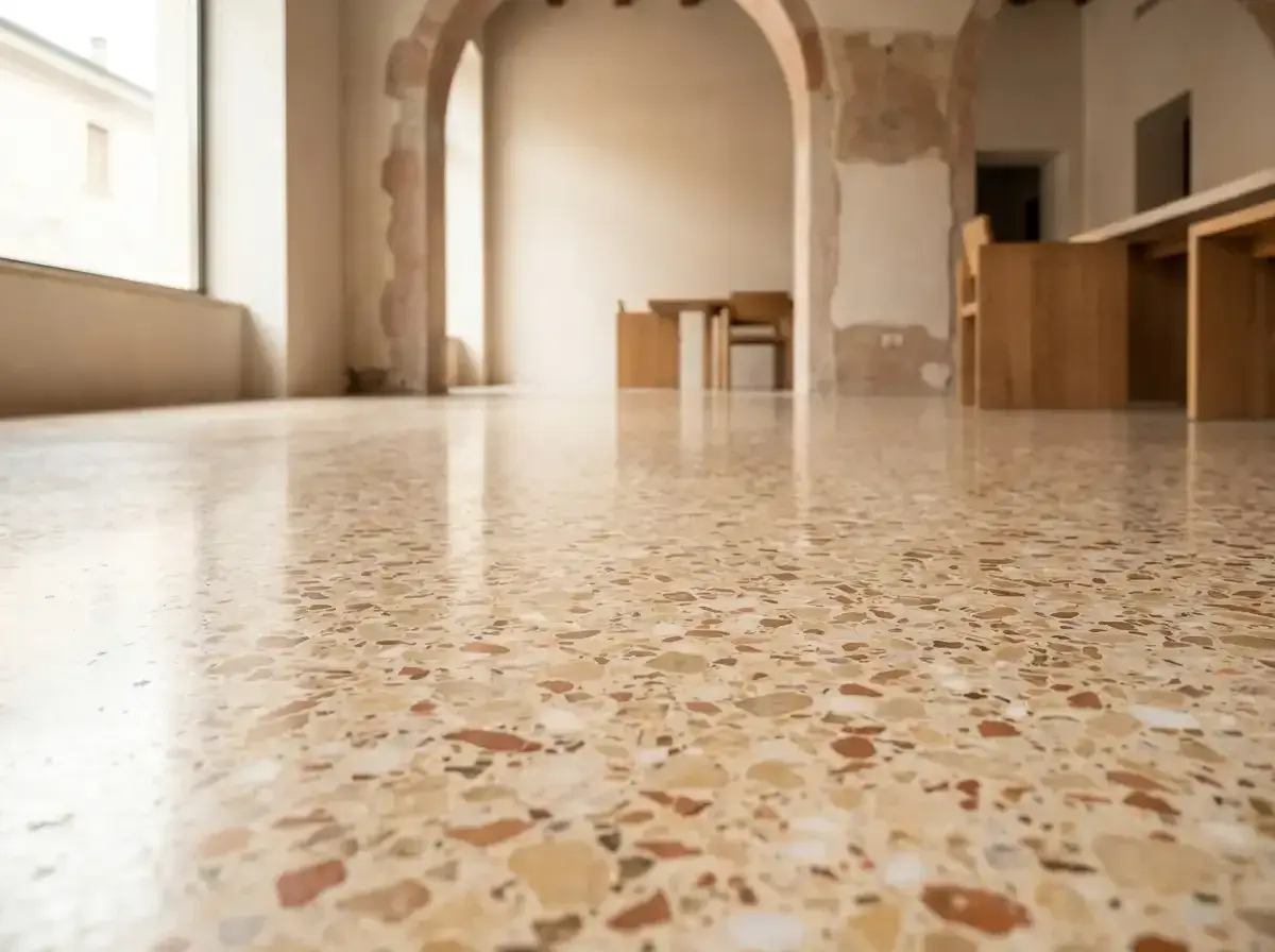 Pavimentazione terrazzo lucida con inserti colorati, che riflette la luce in un ambiente con archi e arredi in legno.