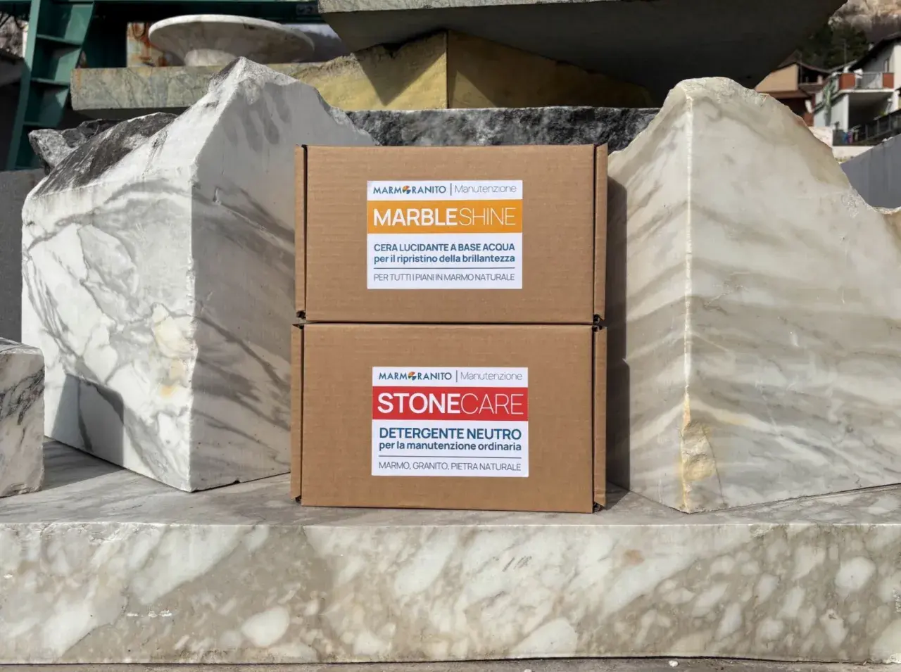 Due scatole di prodotti per la pulizia del marmo, "MarbleShine" e "Stonecare", sono posizionate tra blocchi di marmo grezzo. Ideale per sapere come lavare pavimento in marmo.