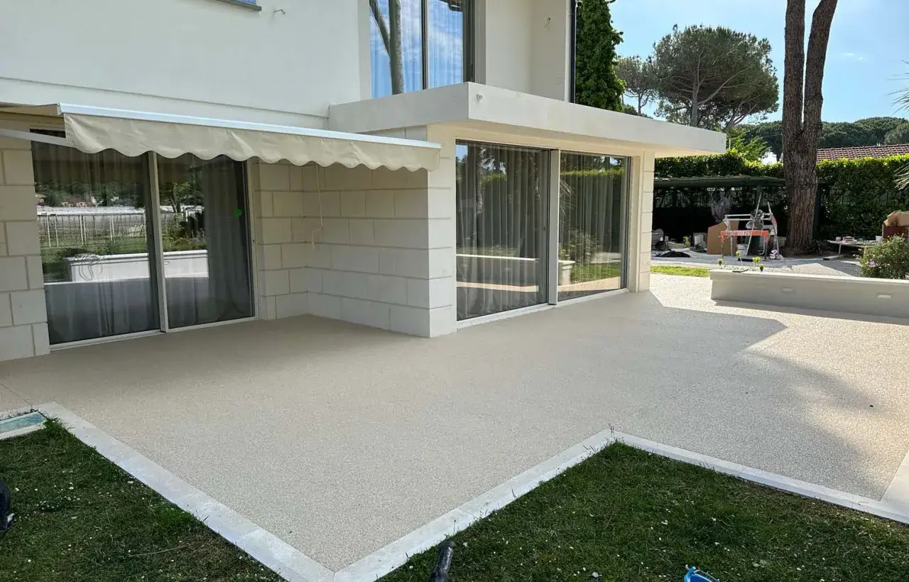 Terrazza moderna con pavimentazione in ghiaia stabilizzata, che si estende dal patio fino al giardino verdeggiante.
