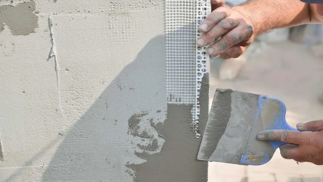 Mani esperte applicano intonaco su una rete per stuccare muro, creando una superficie liscia e uniforme.