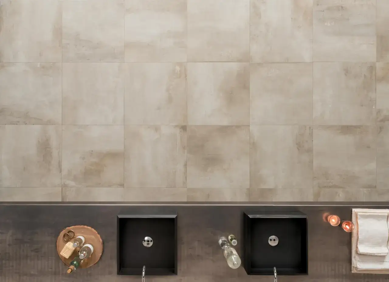 Bagno moderno con due lavabi neri, accessori e un'elegante parete rivestita in gres tutta massa color sabbia.