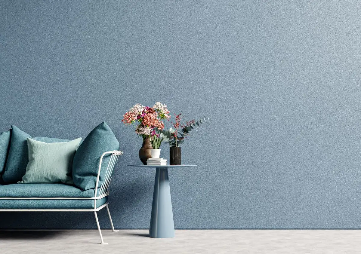 Divano blu e tavolino con fiori su parete con effetti pittura pareti moderne.