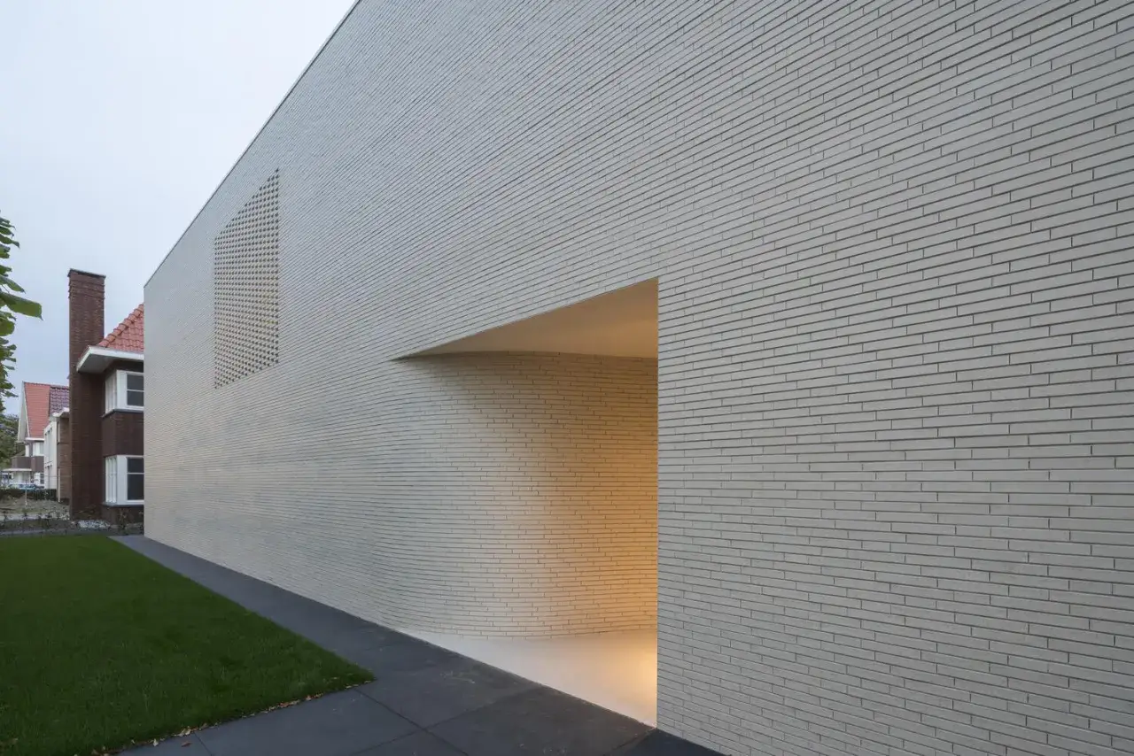 Muro moderno in mattoni chiari, con un'apertura ad arco e una finestra decorativa. Esempi di tipi di mattoni per muri esterni.