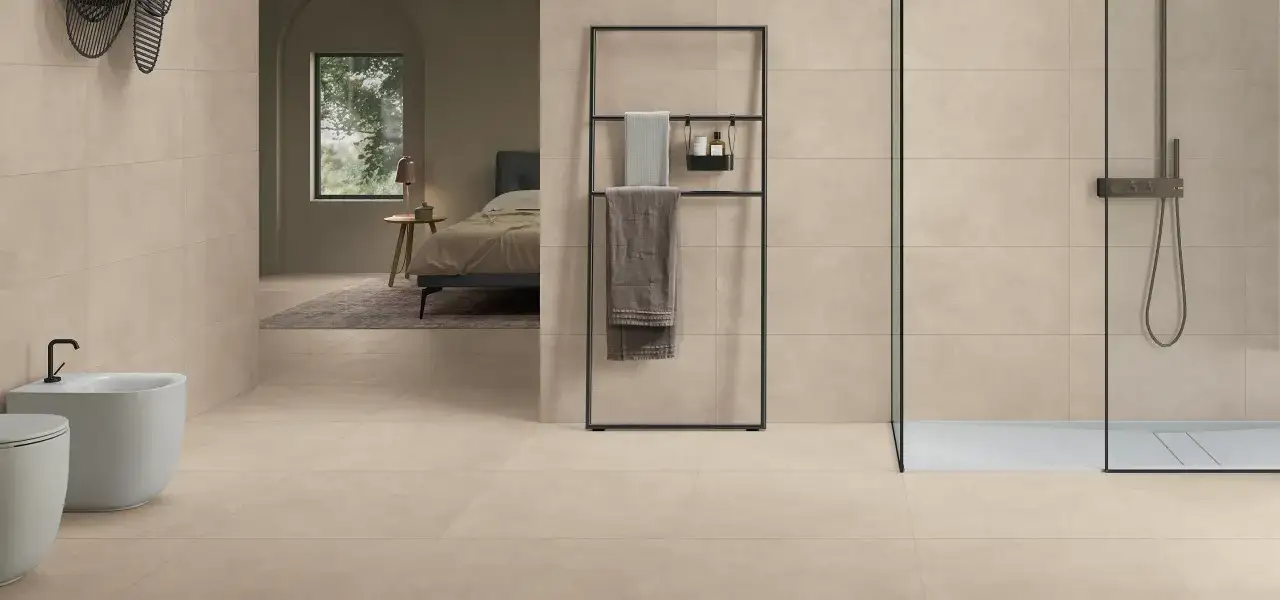Elegante bagno con finiture in resina e piastrelle color sabbia, con bidet, doccia e un'apertura verso una camera da letto.