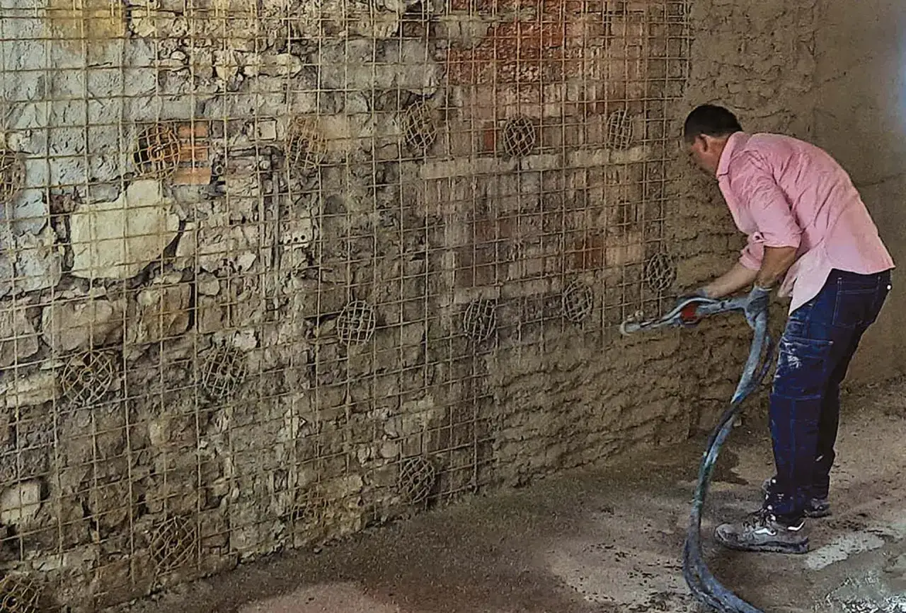 Operaio applica intonaco armato con rete in fibra di vetro su un muro grezzo.