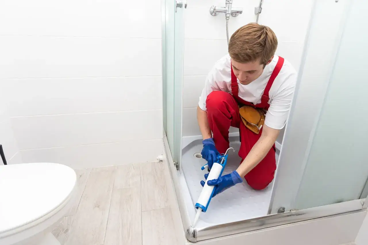 Un operaio usa il silicone per box doccia per sigillare la base della doccia, garantendo un ambiente asciutto e sicuro.