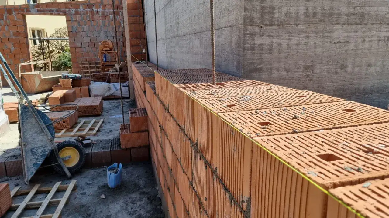 Cantiere edile con mattoni rossi in fase di posa. La costruzione di muri in laterizio contribuisce all'embodied carbon.