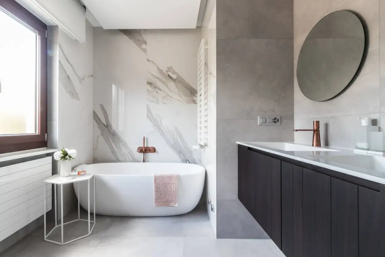 Bagno moderno con vasca freestanding, rubinetteria in rame e rivestimento bagno uguale al pavimento in gres effetto marmo e cemento.