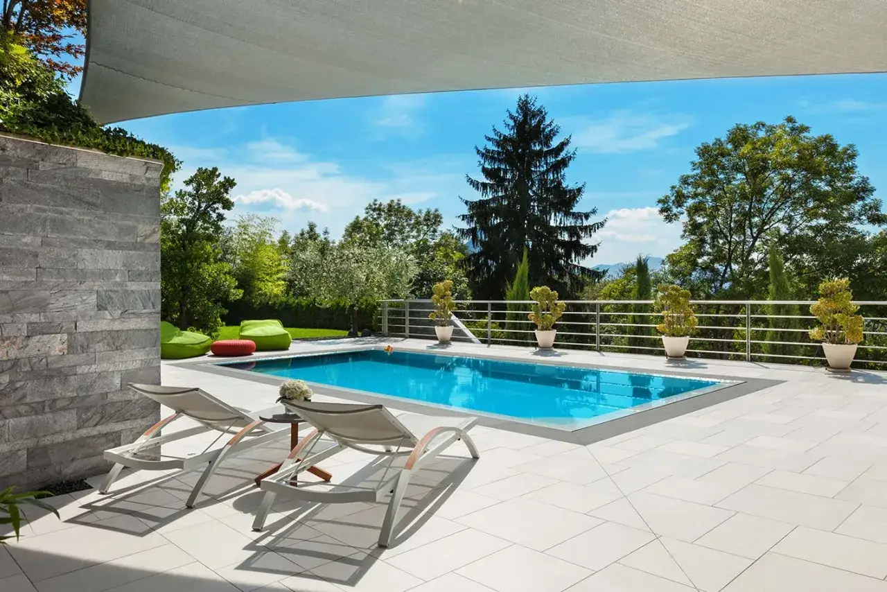 Piscina azzurra con lettini e piante, pronta per l'estate. La manutenzione piscina &egrave; fondamentale per godersi questo angolo di paradiso.