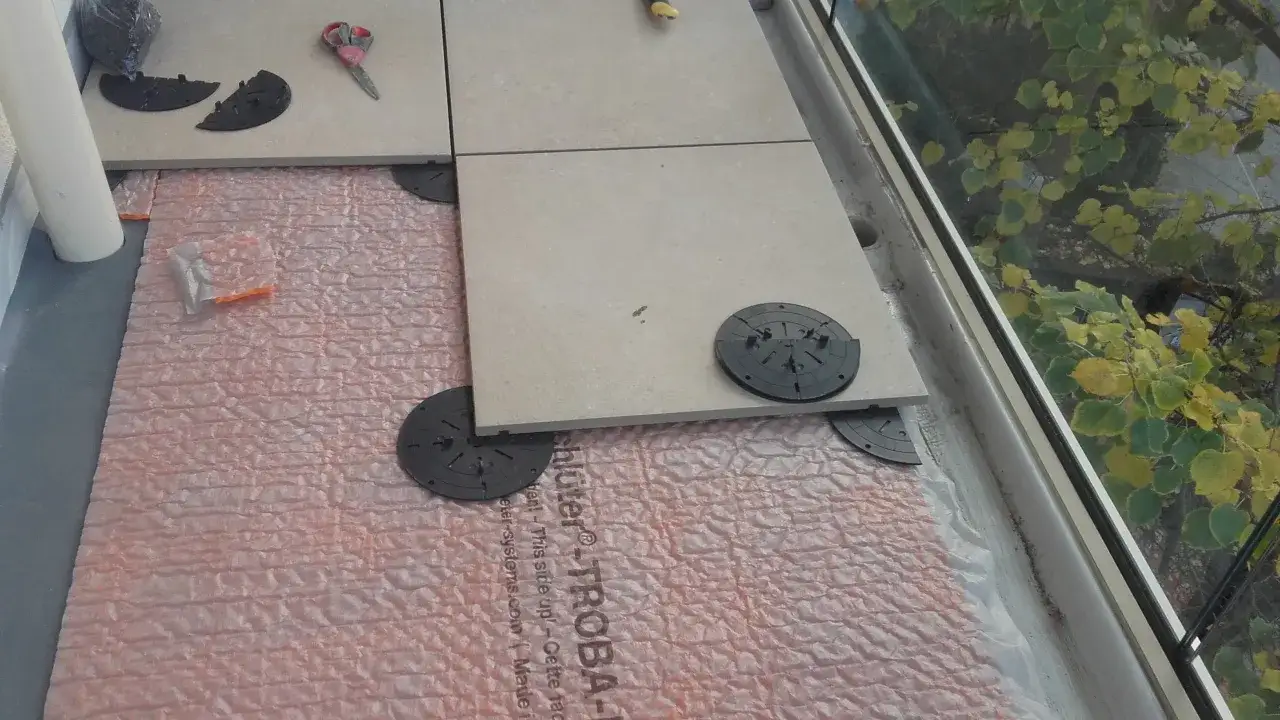 Installazione di un pavimento galleggiante su guaina bituminosa, con piastrelle in fase di posa su supporti regolabili.