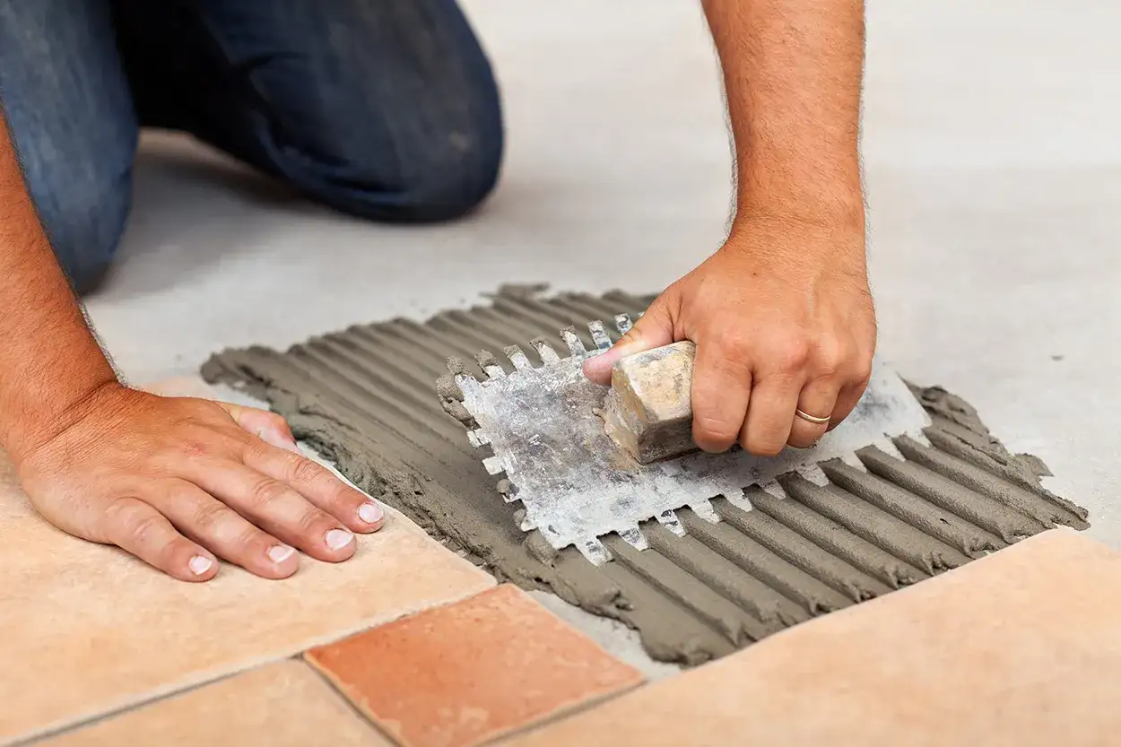 Mani esperte stendono la colla per piastrelle con una spatola dentata, assicurando la giusta quantità al metro quadro per una posa perfetta.