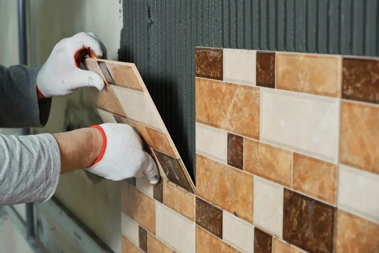 Mani guantate posano piastrelle effetto marmo su muro con colla. Un progetto di piastrelle bagno fai da te in corso.