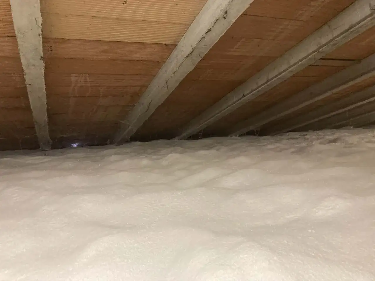 Spessore isolamento sottotetto non abitabile con schiuma espansa. Il soffitto in legno è visibile sopra la soffice coltre bianca.