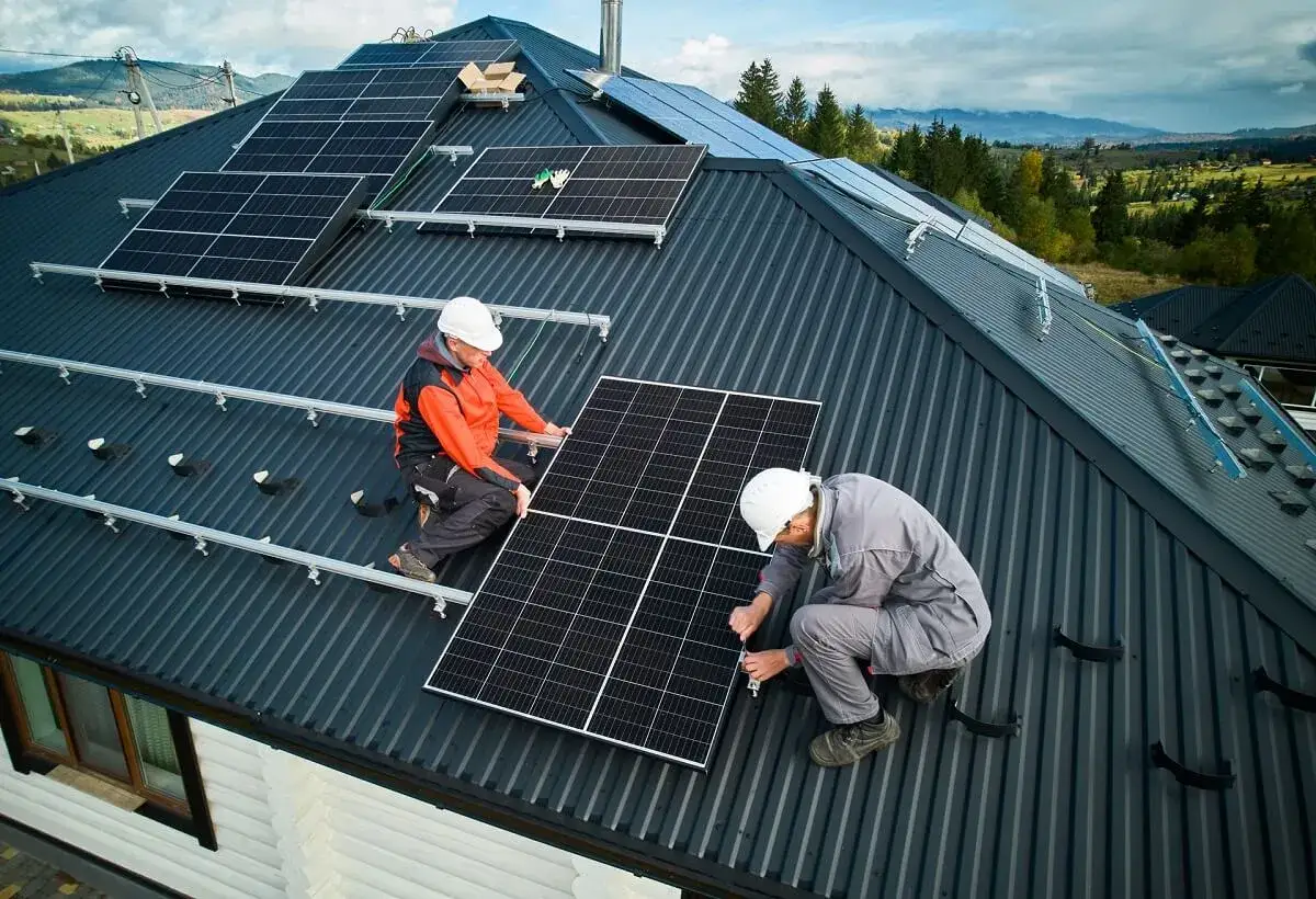 Installatori al lavoro sul tetto per il dimensionamento impianto fotovoltaico. Montaggio pannelli solari in un paesaggio collinare.