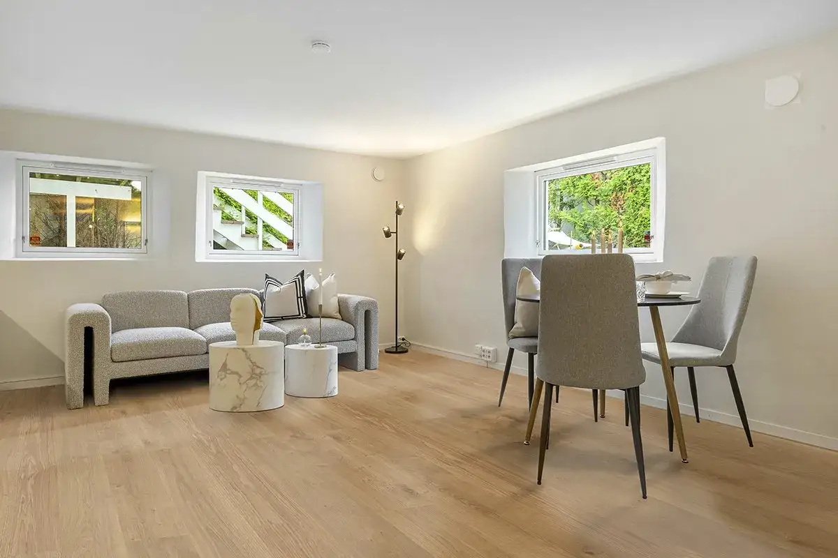 Soggiorno moderno con divano grigio, tavolini rotondi e un tavolo da pranzo. Il pavimento stile nordico in legno chiaro dona calore all'ambiente.